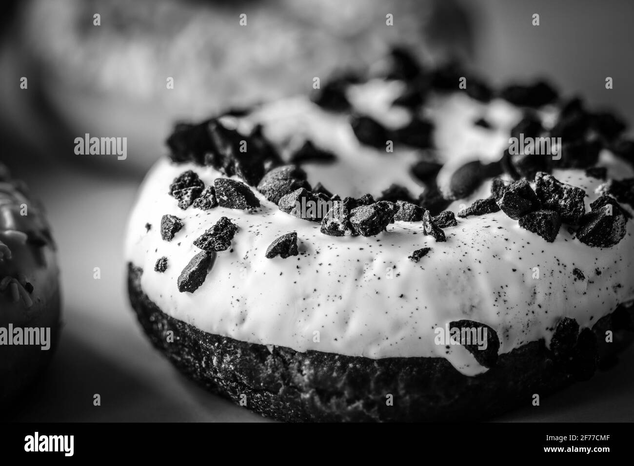 Nahaufnahme von Ringdonut mit weißer Glasur, mit schwarzen Keksen bestreut, monochromes Bild Stockfoto