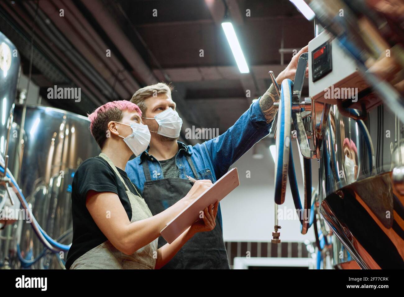 Zwei junge Brauer der modernen Bierfabrik schauen sich an Bedienfeld, während der Mann während der Arbeit in auf Daten zeigt Verarbeitungsanlage Stockfoto
