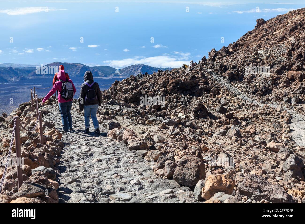 Eine Gruppe von Touristen steigt vom Gipfel des Teide-Vulkans entlang einer Steintreppe zwischen dem Lavahaufen herab. Drei Personen in winddichter Kleidung wanderten Stockfoto