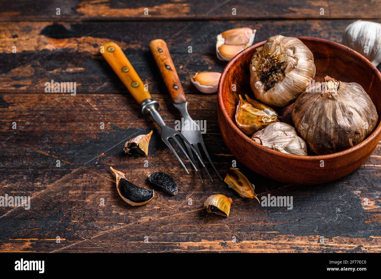 Bulbs and cloves of fermented black garlic in a plate. Dark wooden background. Top view. Copy space Stockfoto