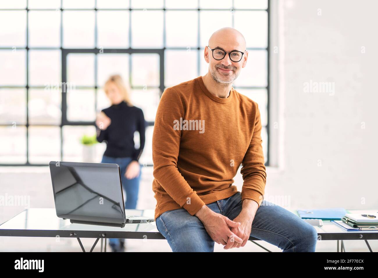 Portait Aufnahme eines lächelnden Geschäftsmannes, der die Kamera ansah und legere Kleidung trug, während er am Schreibtisch im Büro saß. Stockfoto