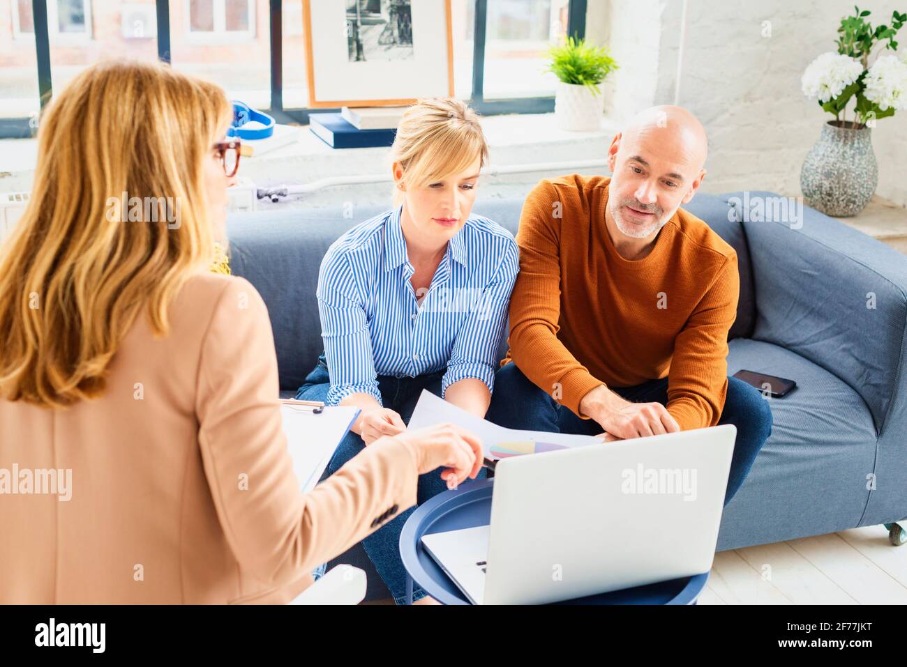 Glückliches Paar, das mit ihrem Finanzberater kommuniziert, während es zu Hause im Wohnzimmer sitzt. Stockfoto