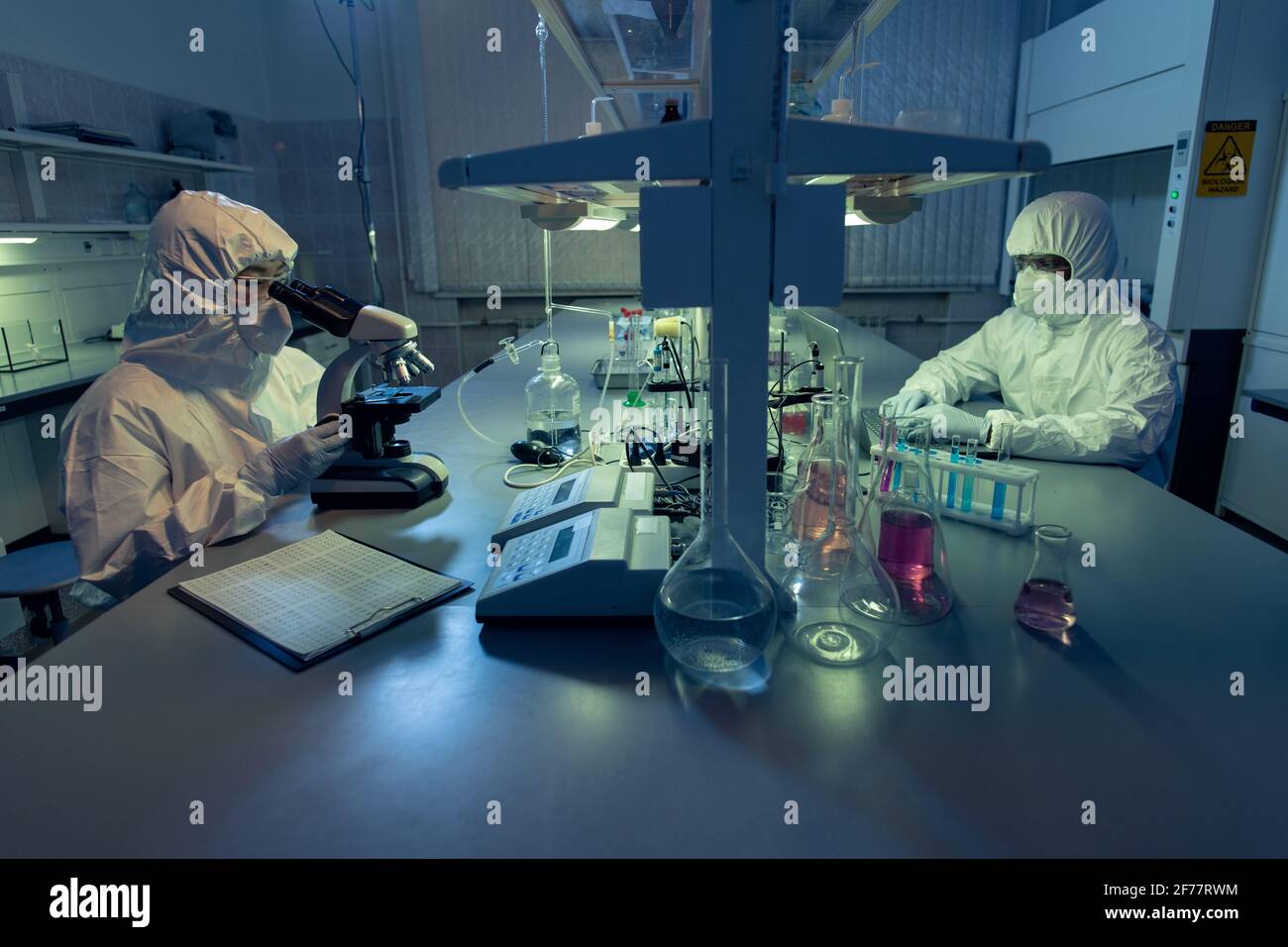 Zwei Kollegen in schützender Arbeitskleidung sitzen am Tisch und Arbeiten mit chemischen Proben in Reagenzgläsern im Laoratorium Stockfoto