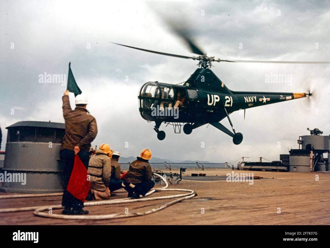 USS New Jersey (BB-62) EIN Sikorsky HO3S-1 Hubschrauber der Staffel HU-1 hebt vom Nachdeck des Schlachtschiffes ab, während sie vor Korea operieren musste. Die hochgelobte grüne Flagge bedeutet, dass der Pilot die Startgenehmigung hat. Die Crash-Crew, in gelben Helmen, steht mit Feuerwehrschläuchen bereit. Das Foto datiert vom 14. April 1953. Fotograf ist LT. R.C. Timm. Offizielles US-Navy-Foto Stockfoto