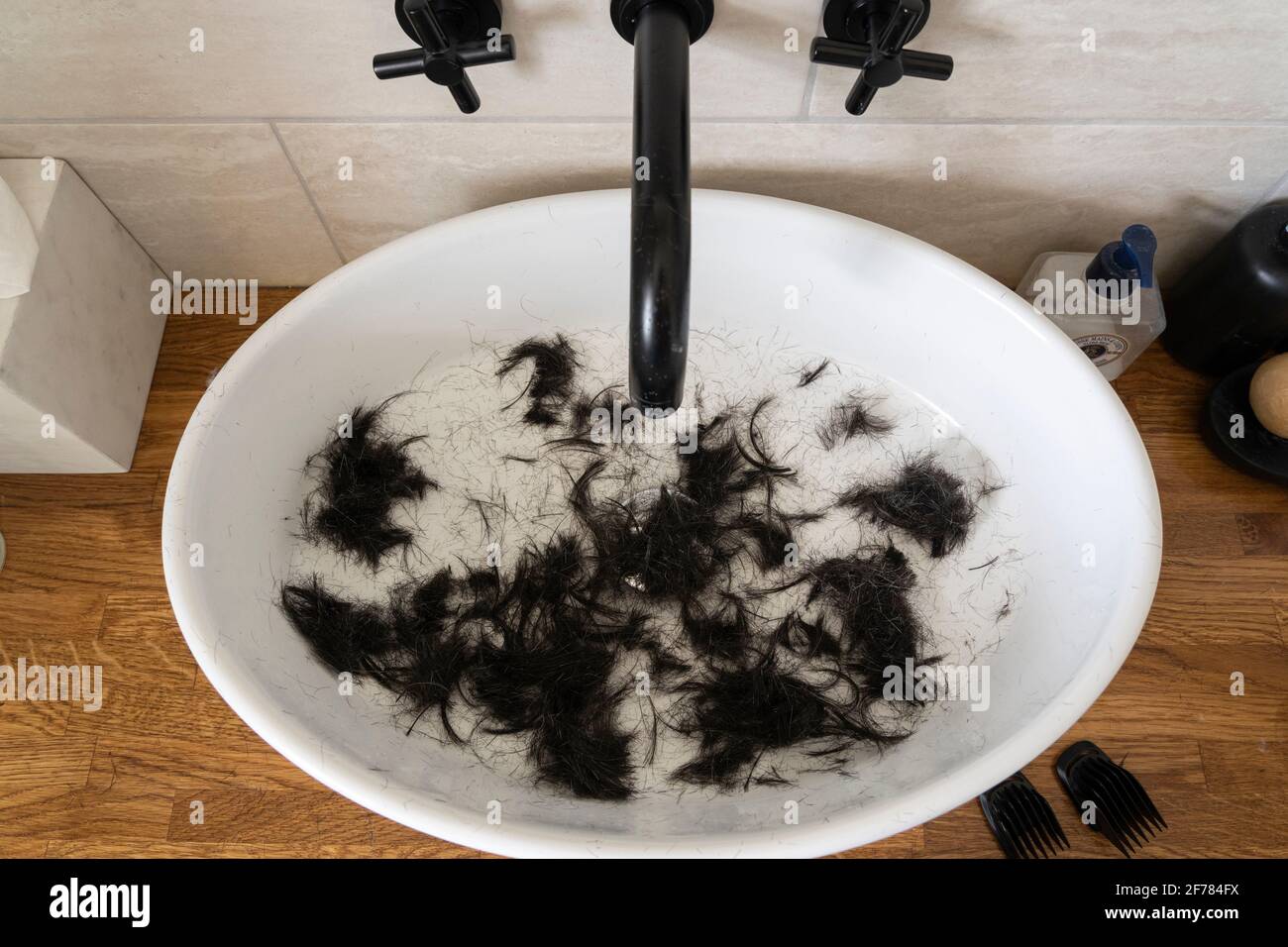 Weißes Porzellanbecken voll dunkelbraunem, frisch geschnittenem Männerhaar, nachdem er während der Coronavirus-Pandemie Covid-19, Großbritannien, mit Haarschneidemaschinen sein eigenes Haar geschnitten hatte Stockfoto