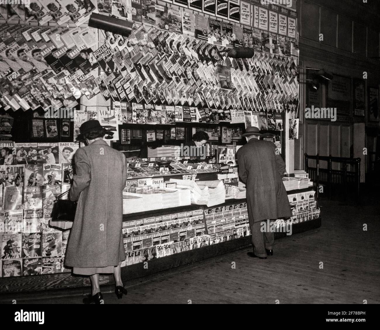 1940ER-JAHRE ANONYME FRAU UND MANN BEI DER AUSWAHL DES EINKAUFS PUBLIKATIONEN BÜCHER UND ZEITUNGEN AN GUT SORTIERTEN ZEITUNGSKIOSKS - R1854 HAR001 HARS DAMEN PERSONEN MÄNNER ZEITUNGEN B&W SHOPPER SHOPPER PENDLER DISCOVERY KUNDENDIENST UND CHOICE AUSSENNEWSSTAND – GELEGENHEIT ZUR RÜCKANSICHT ZEITSCHRIFTEN BERUFE BAHNHOF BEQUEM VON HINTER KIOSK RÜCKANSICHT PAPERBACK SCHWARZ-WEISS CONVENIENCE HAR001 ALTMODISCHE ZEITSCHRIFTEN GEDRUCKT Stockfoto