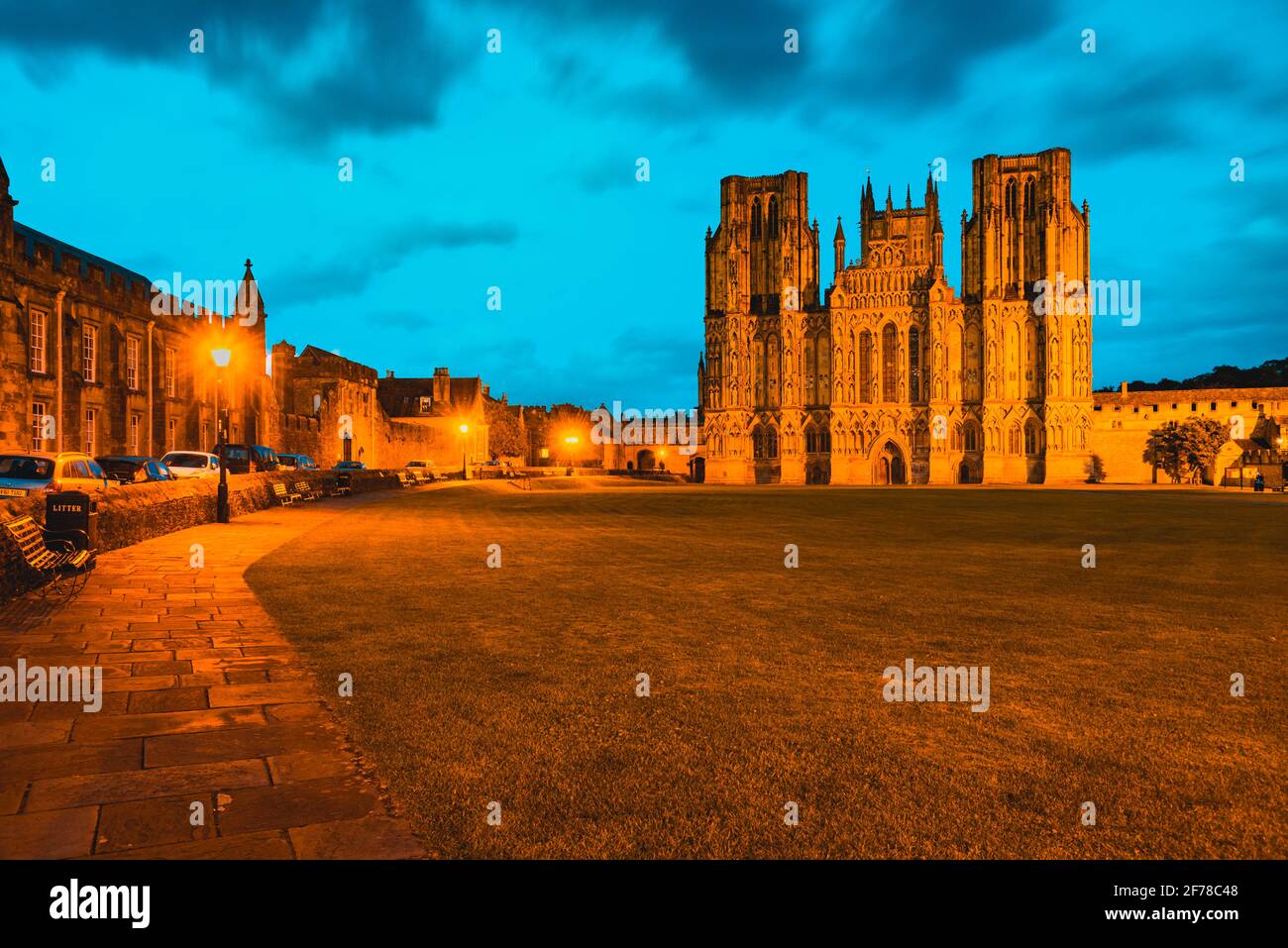 Wells Cathedral in Somerset England mit orangefarbenen Lichtern, die das erhellen westliche Front des frühenglischen gotischen Bauwerks und der Grün vorne Stockfoto