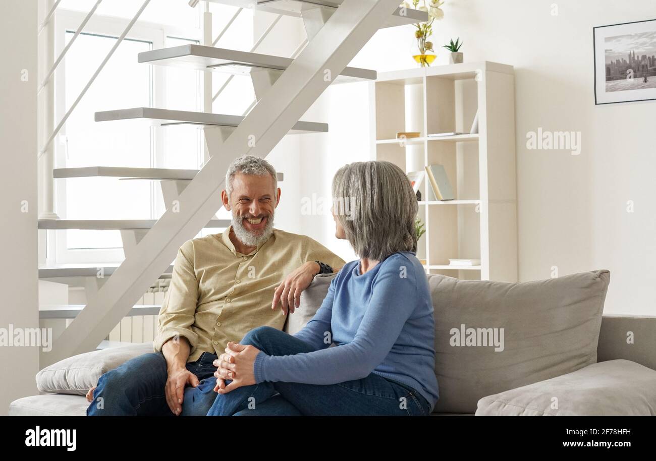 Glückliches reifes älteres Paar, das lachend und sprechend zu Hause auf der Couch sitzt. Stockfoto