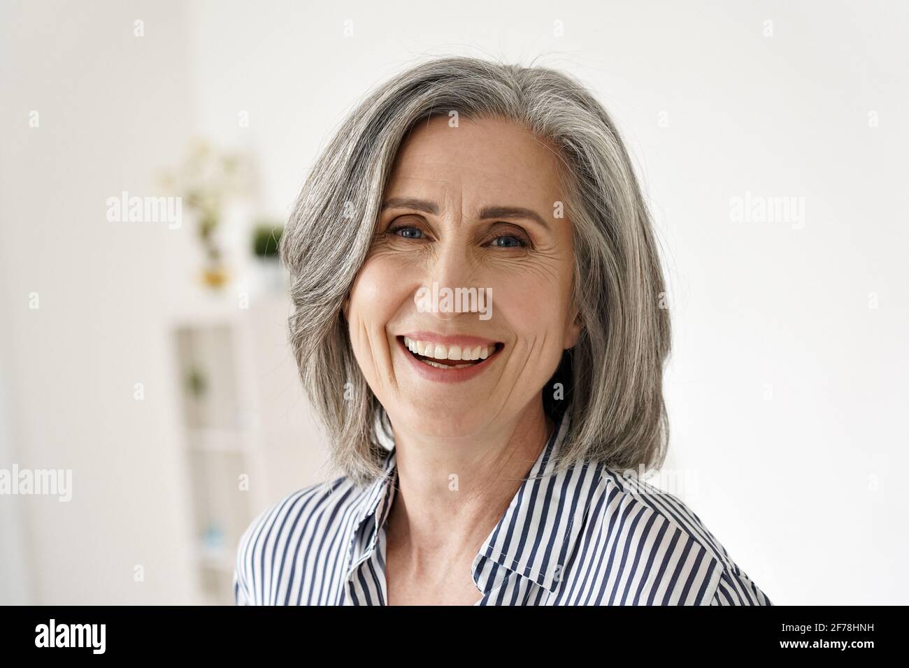 Fröhliche, glückliche, reife Frau aus den 50er Jahren, die lachend die Kamera zu Hause anschaut. Stockfoto