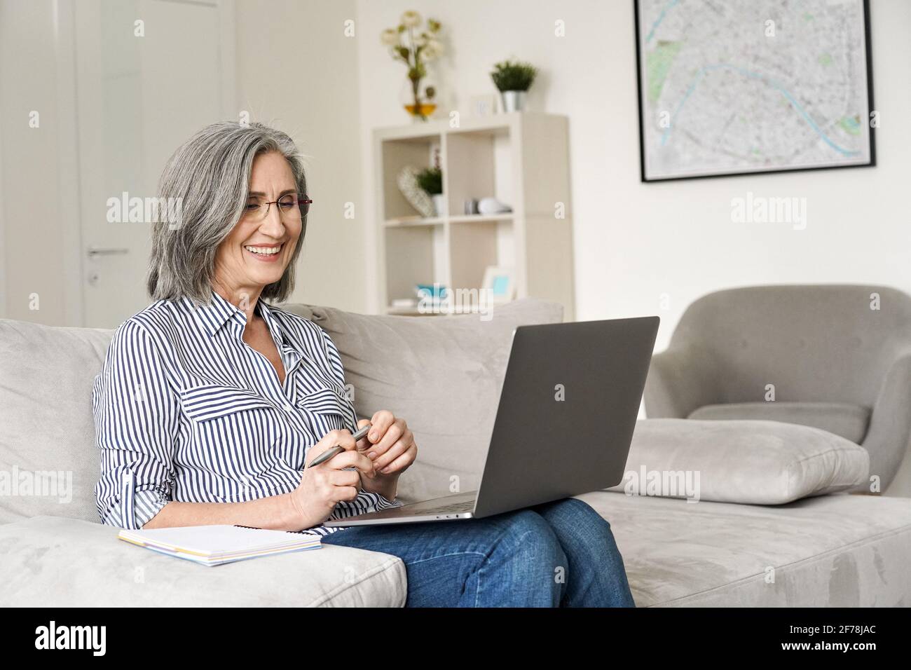 Glückliche ältere Frau im mittleren Alter, die vom Heimbüro aus an einem Laptop arbeitet. Stockfoto