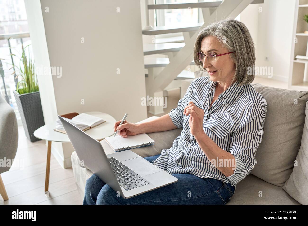 Ältere Erwachsene alte professionelle Frau, die sich zu Hause ein Schulungswebinar auf einem Laptop ansieht. Stockfoto