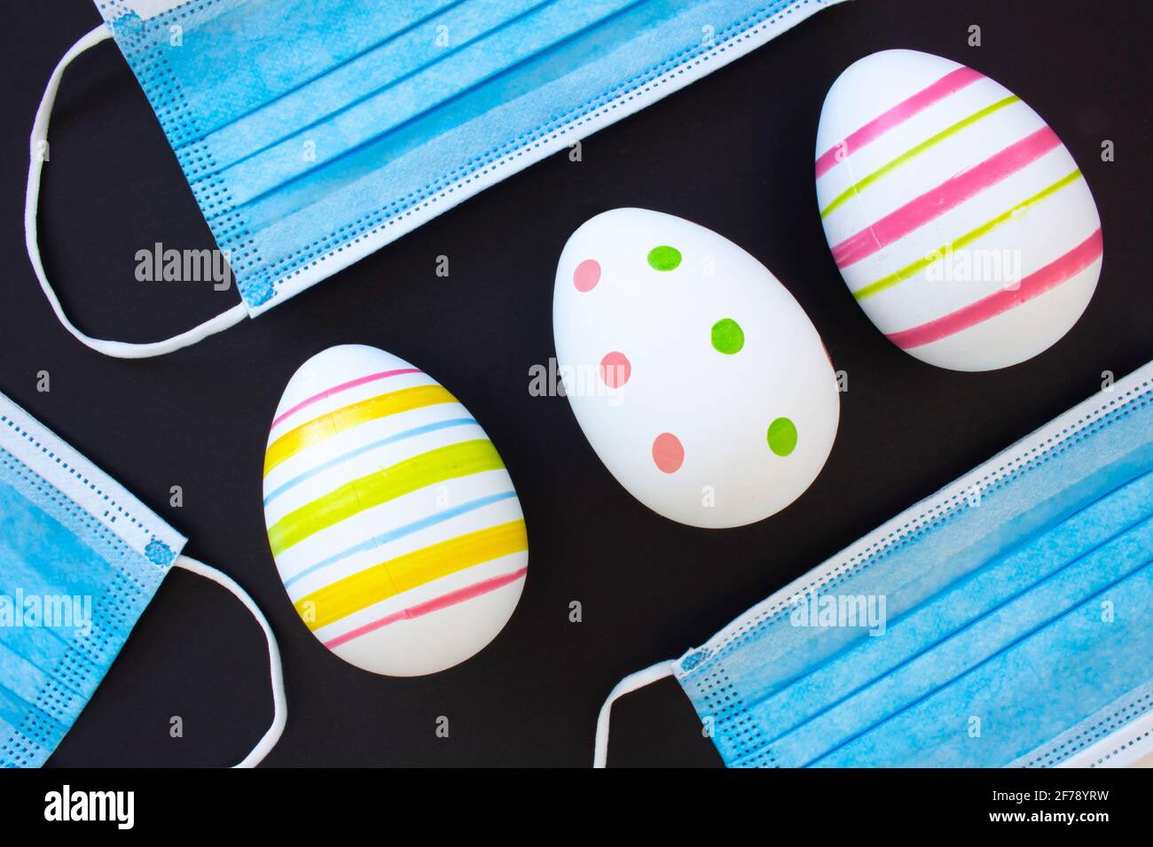 Dekorieren Sie Ostereier mit chirurgischen Gesichtsmasken auf schwarzem Hintergrund. Konzept: Ostern während der Covid-19-Pandemie Stockfoto