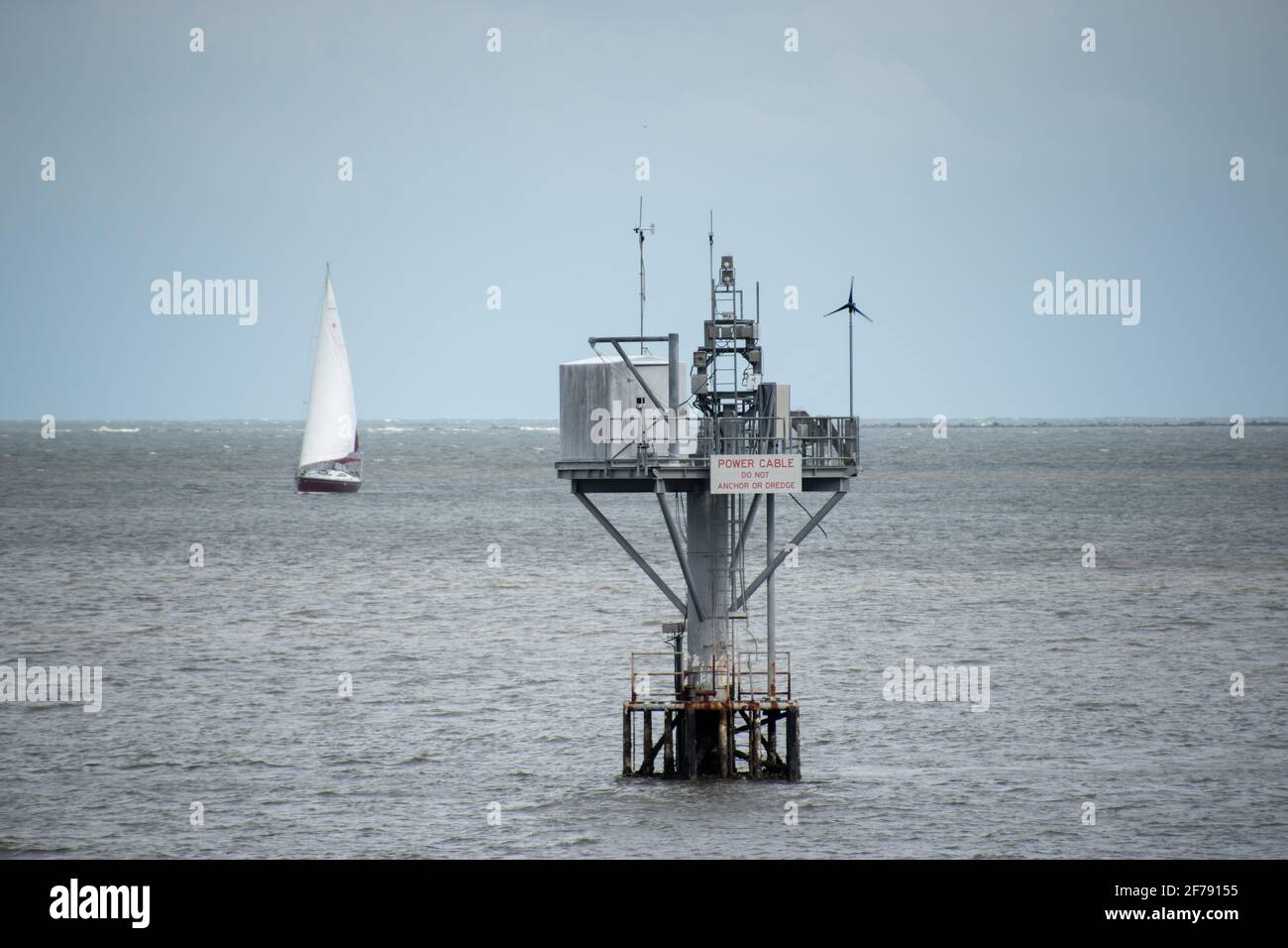 Ein Unterwasser-Stromkabelpier im Charleston Hafen mit Ein Segelboot im Hintergrund Stockfoto