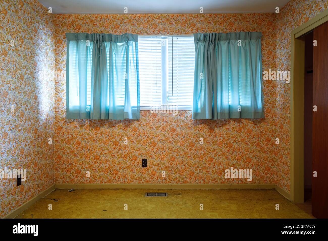 Orangefarbene Retro-Tapete und kontrastierende blaue Vorhänge in einem leeren Schlafzimmer. Stockfoto