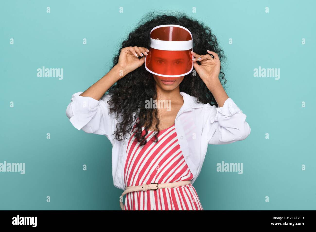 Trendy junge schwarze Mädchen trägt eine transparente rote Spitze oder hut, der in einem durch das Visier auf die Kamera gucken kann Rot-weiß gestreiftes Shirt über einem Türkis Stockfoto