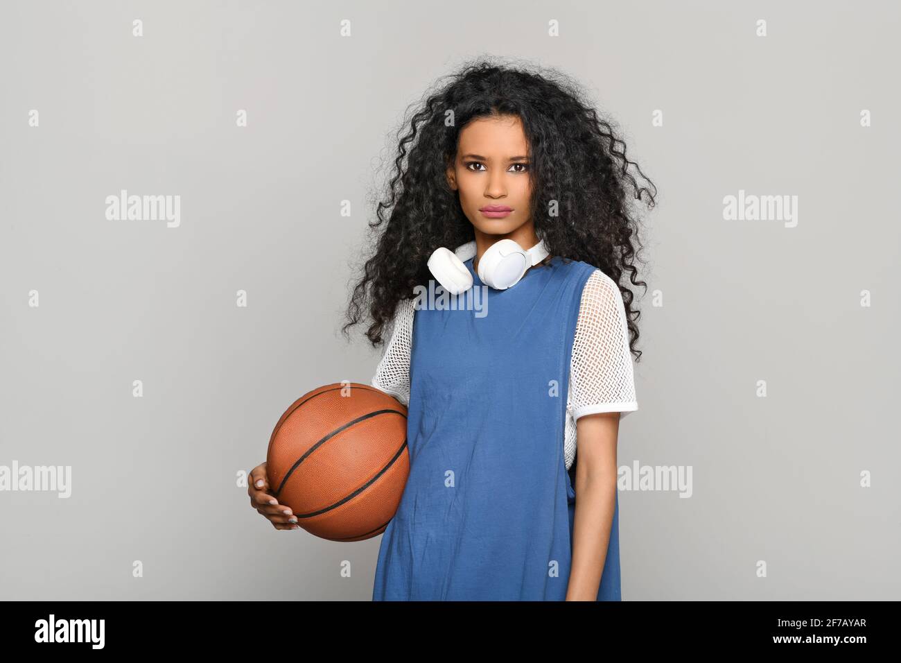 Ziemlich ernst junge Dominikanerin stehend hält einen Basketball suchen Nachdenklich auf die Kamera mit Stereo-Kopfhörern um den Hals Ein Überschuß Stockfoto