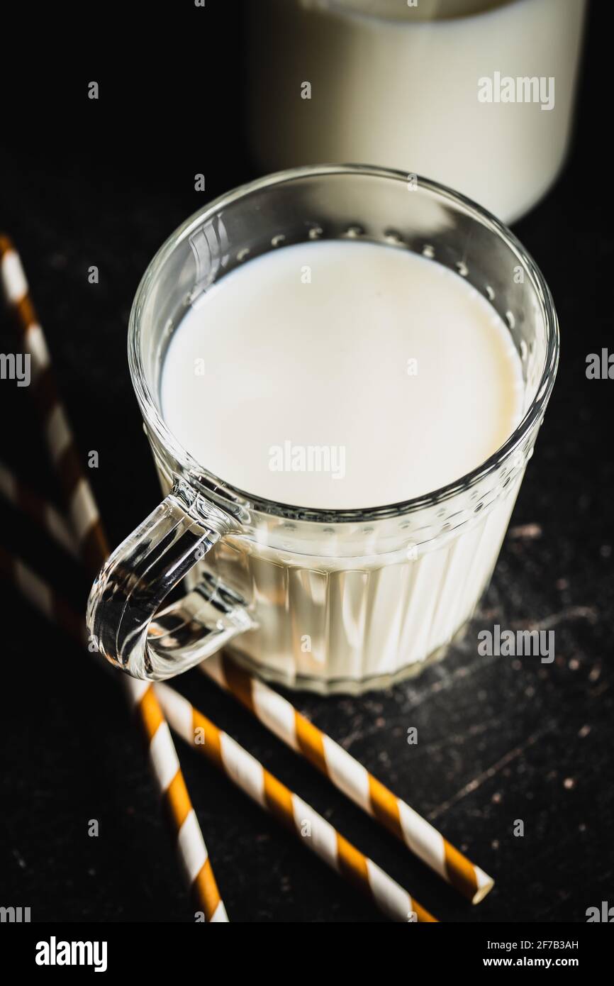 Weiße Milch in Glasbecher auf schwarzem Tisch. Stockfoto