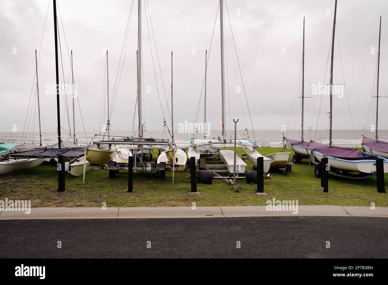 Kleine Segelyachten parkten auf ihren Anhängern auf einer Wiese Patch am Meer an einem regnerischen bewölkten Tag Stockfoto