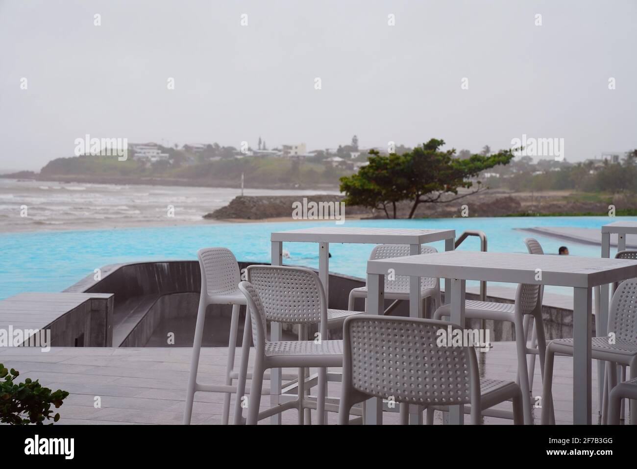 Cafeterische und Stühle neben einem randlosen Pool am ozean an einem nassen und windigen grauen bewölkten Tag Stockfoto