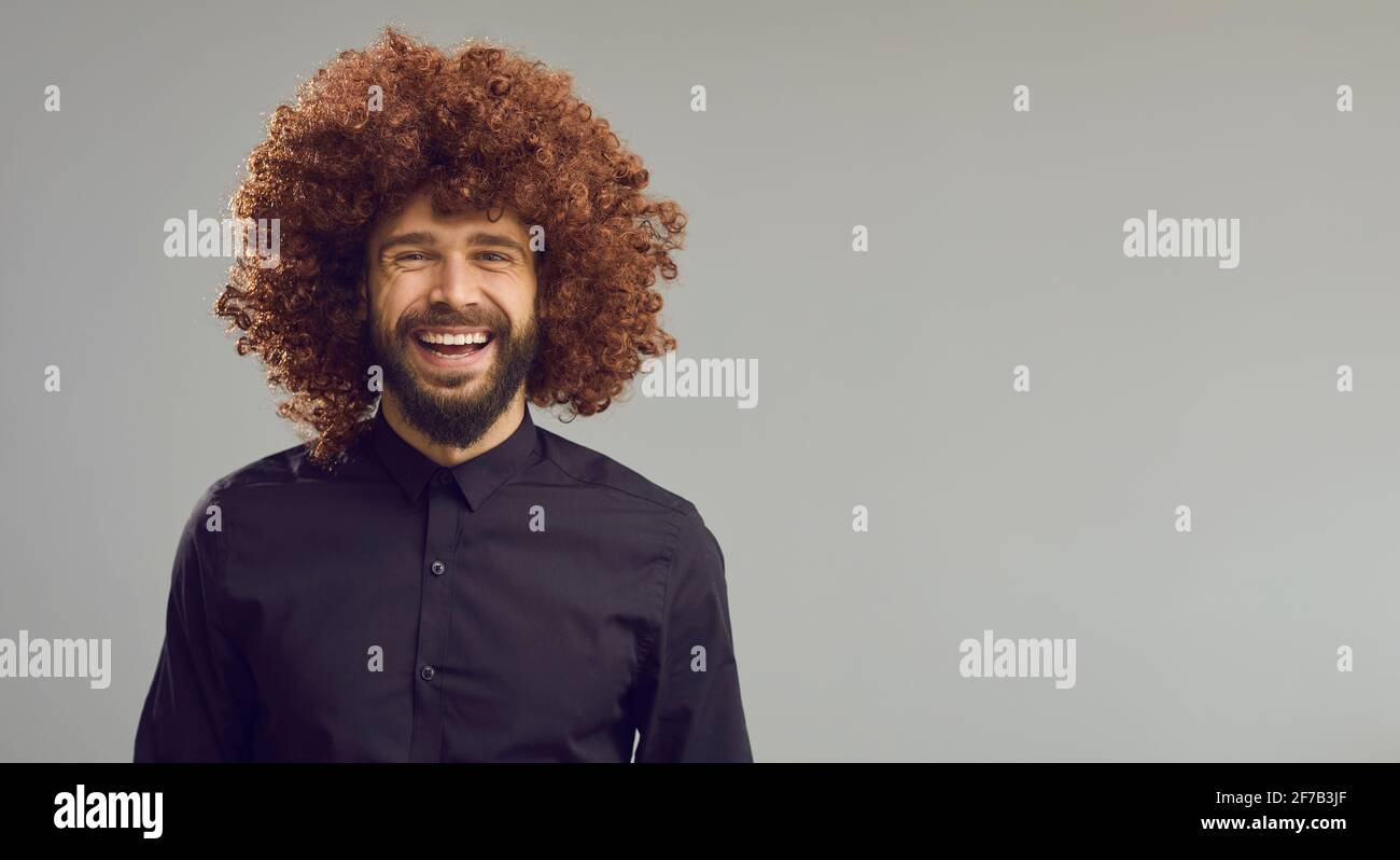 Lustiger Kerl mit dicken lockigen braunen Haaren lachend auf blank Hintergrund für Werbetexte Stockfoto