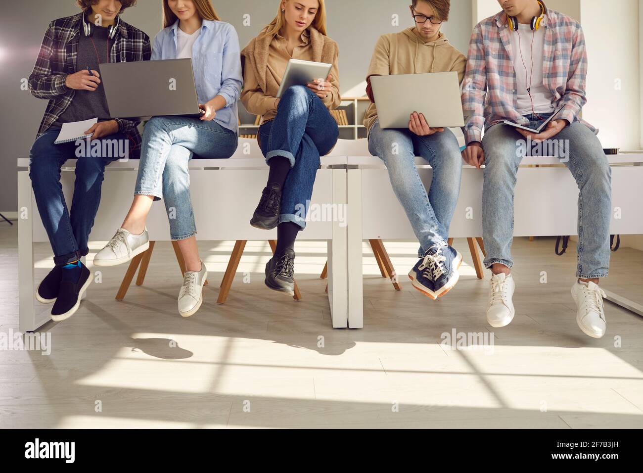 Beschnittenes Bild von Studenten, die mit modernen Geräten auf dem Schreibtisch sitzen und sich auf die Vorträge vorbereiten. Stockfoto