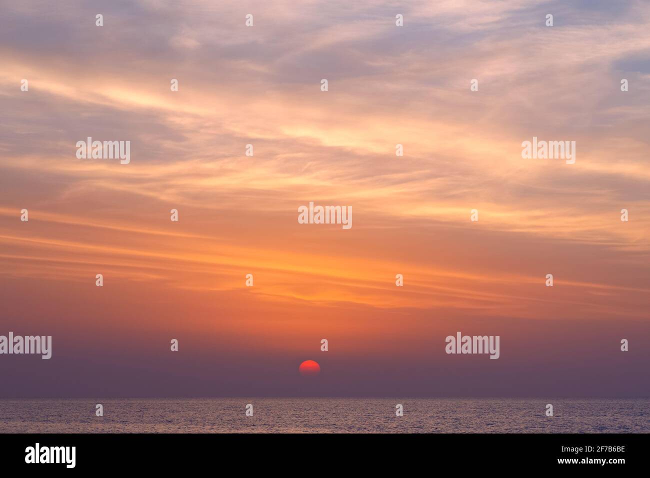 Die Sonne geht bis zum Meereshorizont unter. Heller, wolkiger Sonnenuntergang über der Meereslandschaft. Foto mit weichem Fokus. Stockfoto