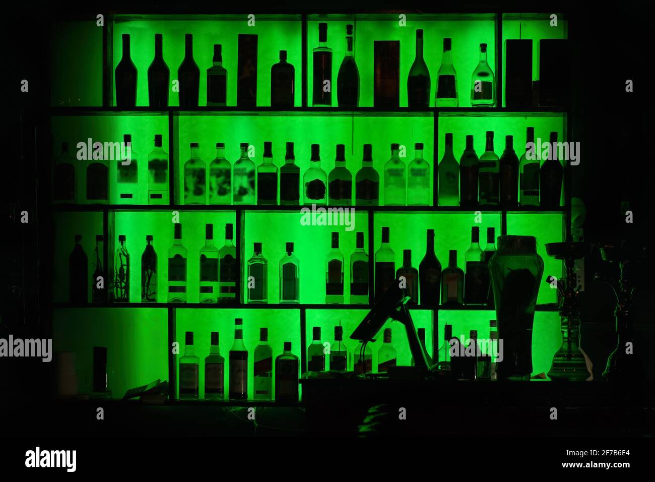 Flaschen mit Alkohol und Spirituosen in Bar- oder Pub-Regalen mit grüner Hintergrundbeleuchtung. Balkenhintergrund. Stockfoto