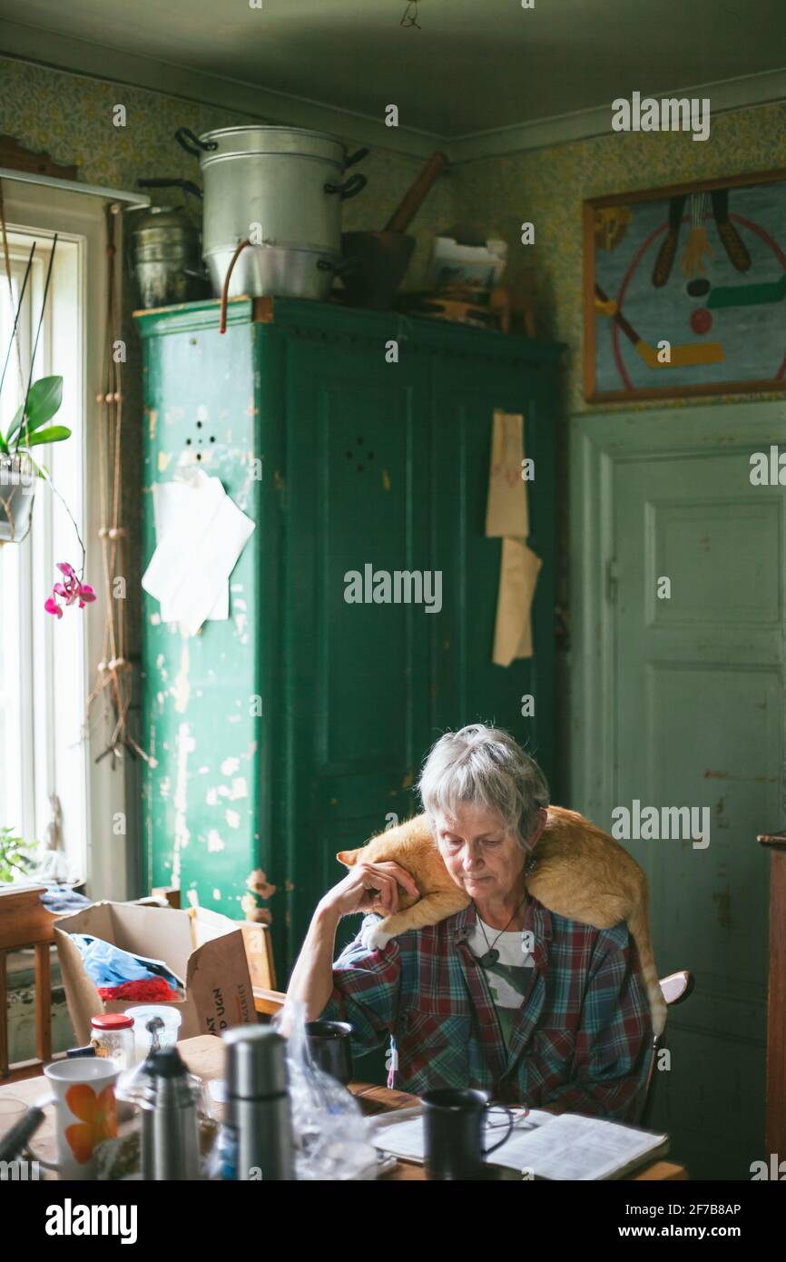 Ältere Frau sitzt am Tisch mit Katze auf ihren Schultern Stockfoto