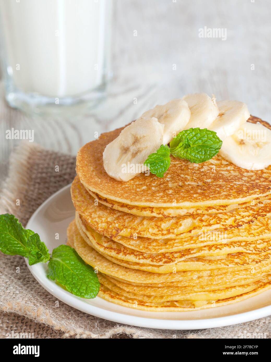 Pfannkuchen mit Milch serviert, garniert mit Minzblättern und Bananenscheiben. Mit Honig oder Ahornsirup gegossen. Stockfoto