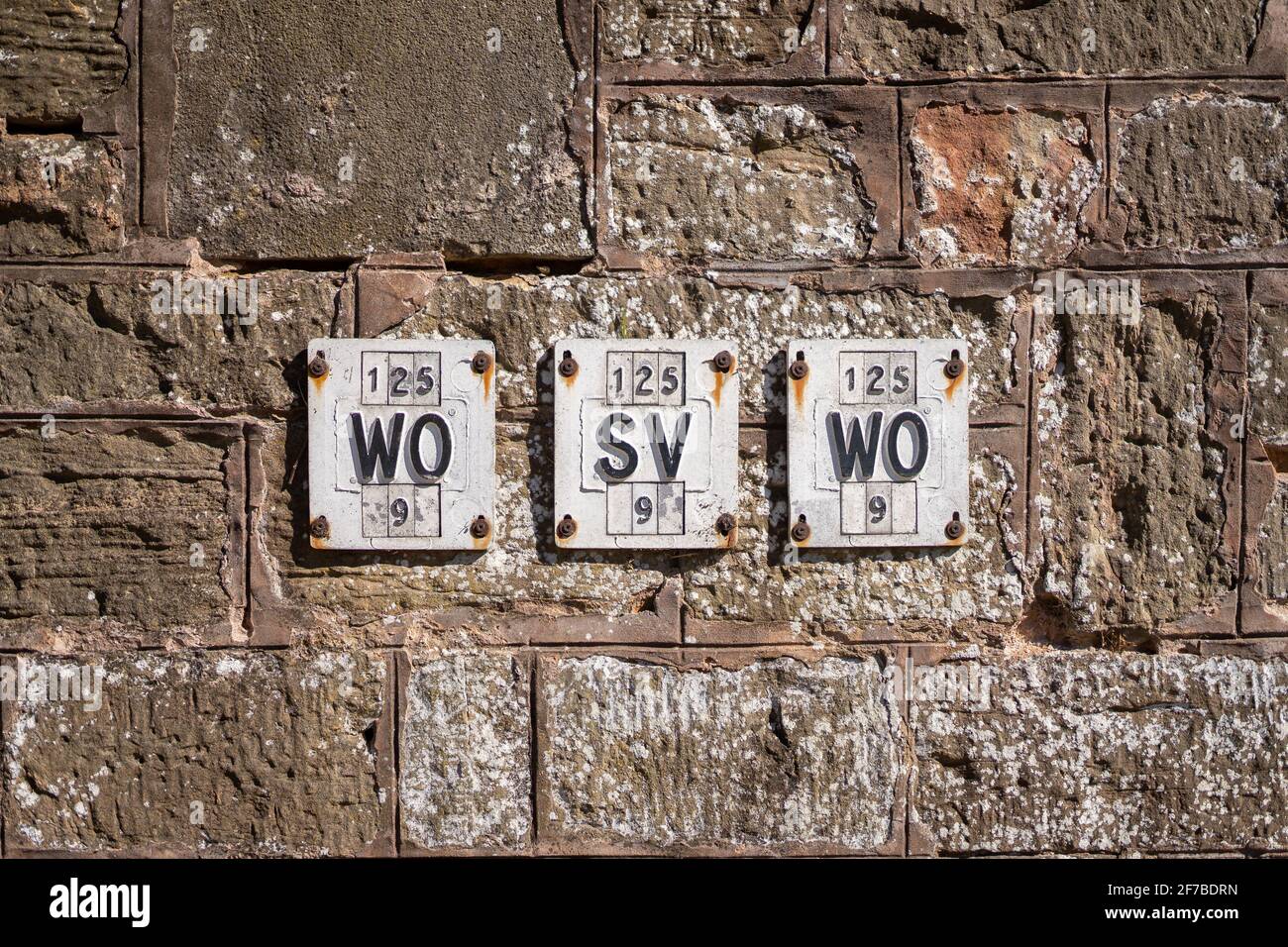 Reihe von alten alten englischen viktorianischen Eisen-Hydranten Schilder auf Stein Granit Wand schwarz und weiß. Symmetrische Reihe von Stahlschildern auf Felsen Stockfoto