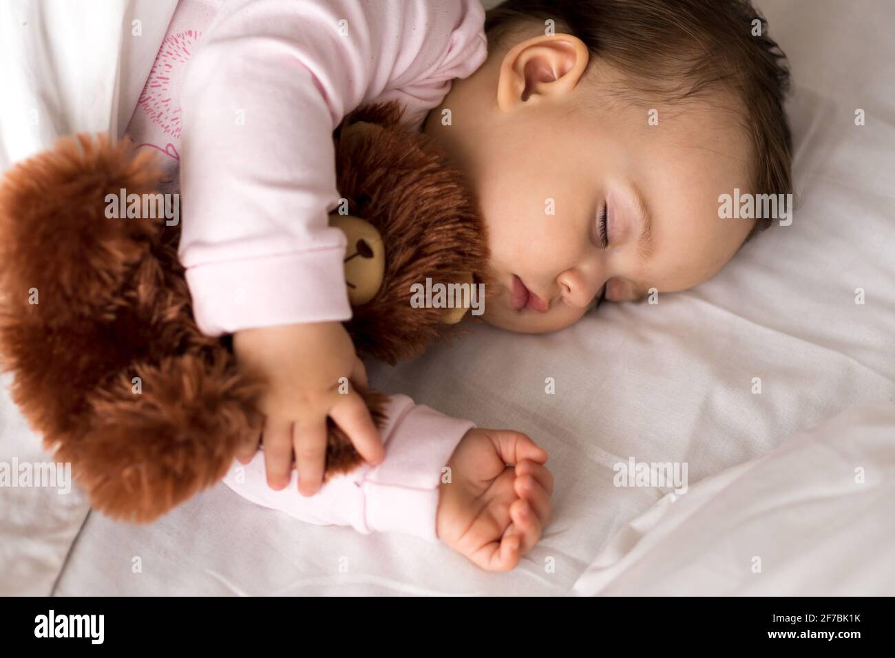 Authentische Porträt niedlichen kaukasischen kleinen Säugling mollig Baby Mädchen oder Jungen in rosa Schlaf mit Teddybär auf weißem Bett. Kind zur Mittagszeit ruhen. Pflege Stockfoto