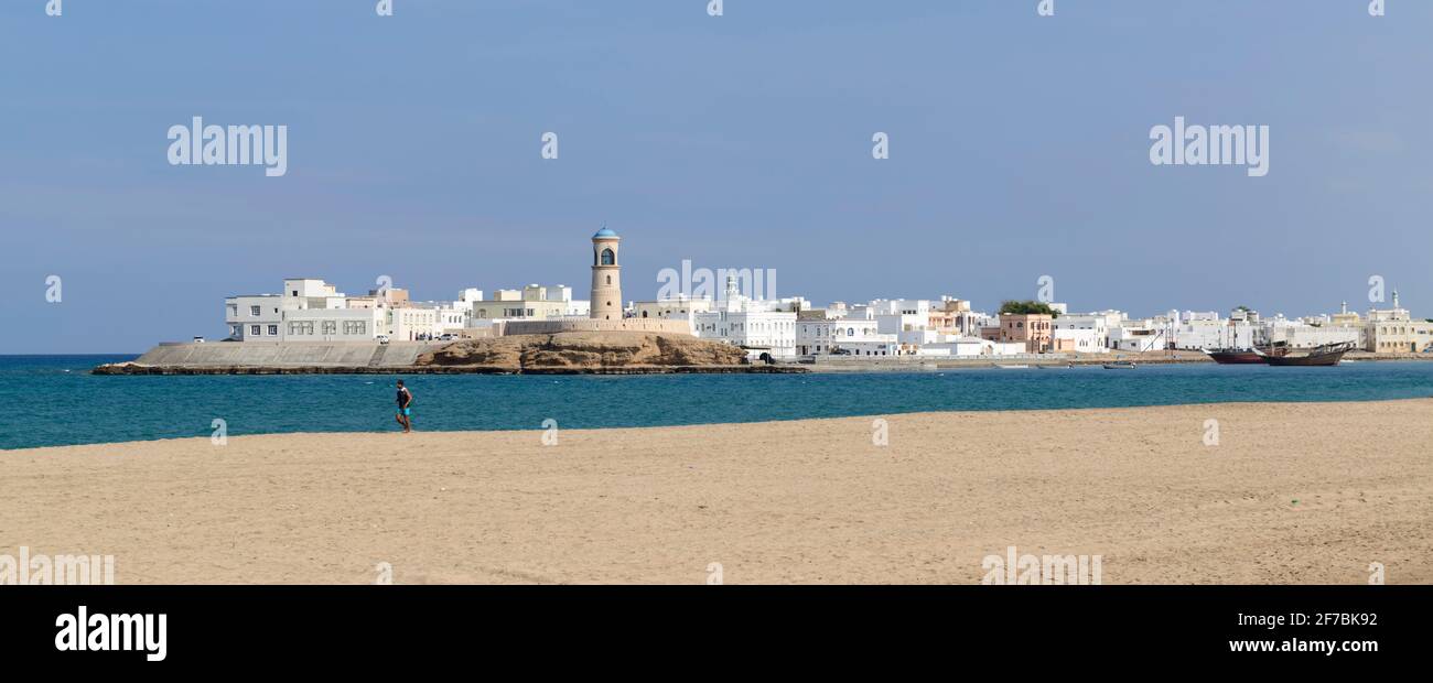 Ein Jogger am Strand von Sur, dem Dorf Ayjah auf der anderen Seite der Lagune. Oman. Stockfoto