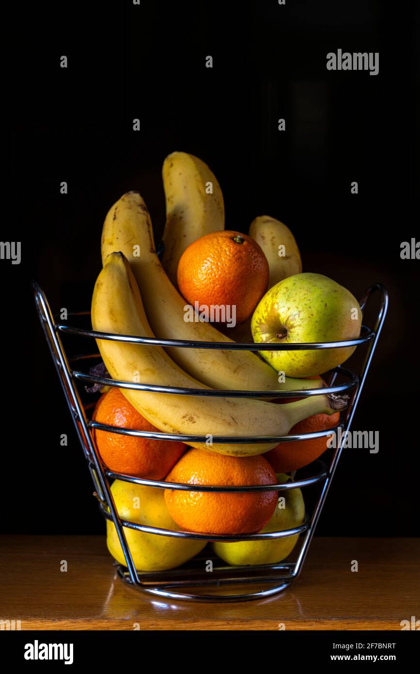 Stillleben von Obstkorb mit Bananen, Äpfeln und Orangen mit schwarzem Hintergrund. Italien, Europa Stockfoto