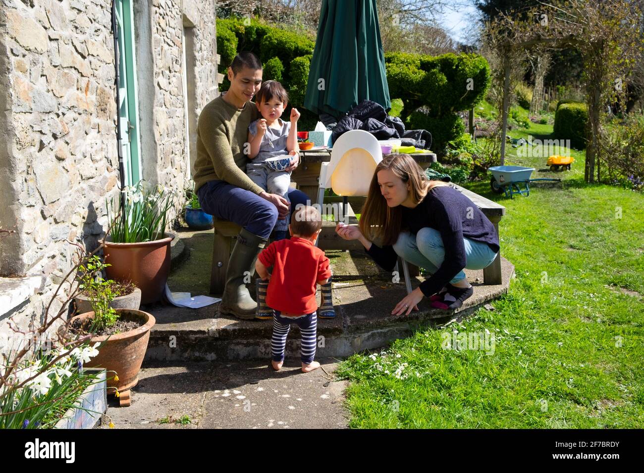Eltern Mutter Vater Familie sitzt mit Kindern vor dem Haus auf Sonniges Osterwochenende in einem Garten in West Wales, Großbritannien KATHY DEWITT Stockfoto
