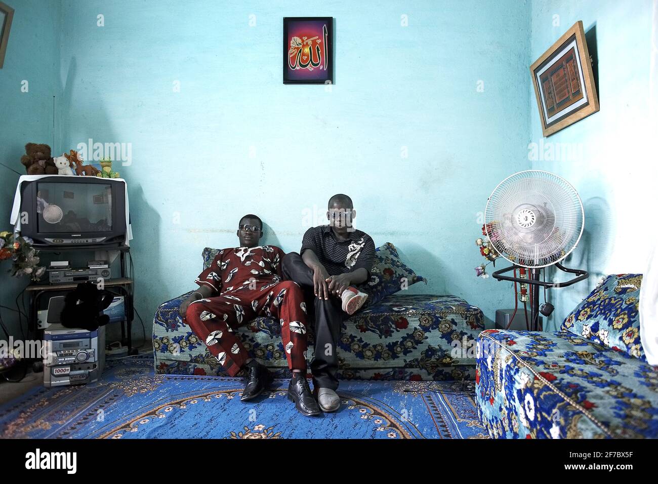 Zwei Mann sitzen auf dem Sofa neben dem Fernseher im Wohnzimmer, Bamako Mali, Westafrika. Stockfoto