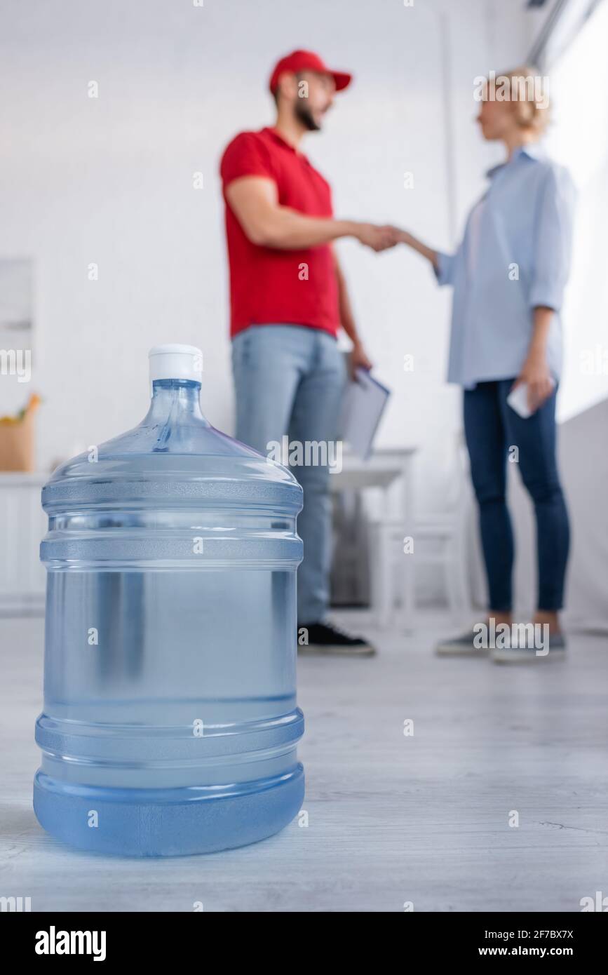 Selektiver Fokus der großen Flasche Trinkwasser in der Nähe von muslim Kurier und Frau schütteln sich die Hände auf unscharfem Hintergrund Stockfoto