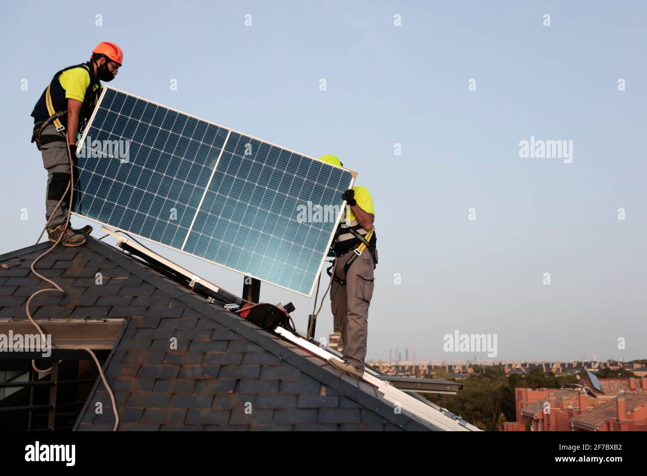 Arbeiter mit Gesichtsmasken installieren Solarzellen auf einem Dach eines Wohnhauses in Majadahonda, Madrid, Spanien. Stockfoto