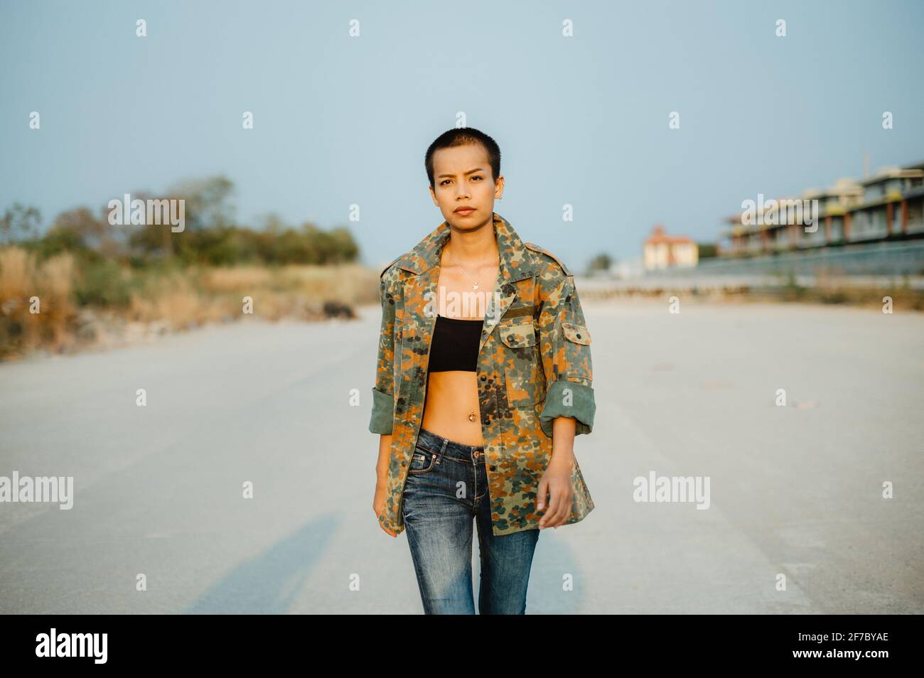 Junge, kurze Haare asiatische Frau trägt Sport-BH und Armee-Jacke, gehen direkt auf die Kamera mit Selbstvertrauen und Entschlossenheit. Stockfoto