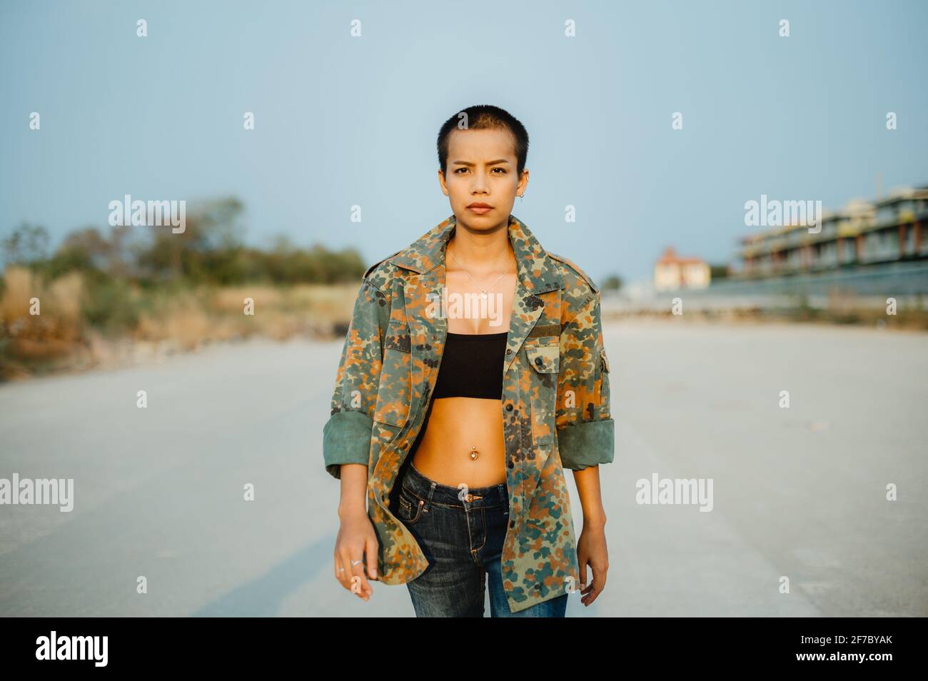 Junge, kurze Haare asiatische Frau trägt Sport-BH und Armee-Jacke, gehen direkt auf die Kamera mit Selbstvertrauen und Entschlossenheit. Stockfoto