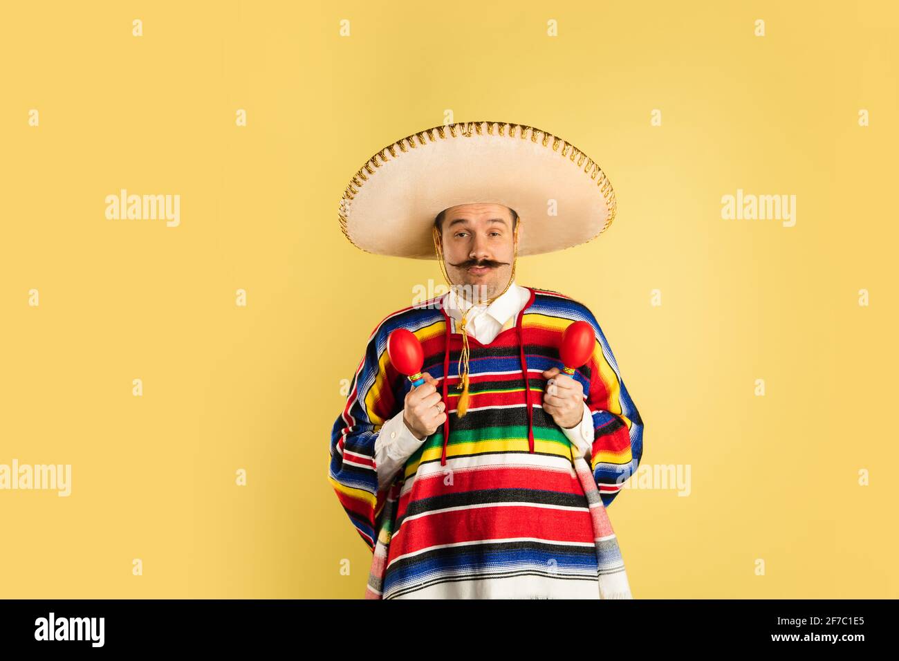 Glücklicher Mann in Sombrero und hellem Poncho über Gelb isoliert Hintergrund Stockfoto