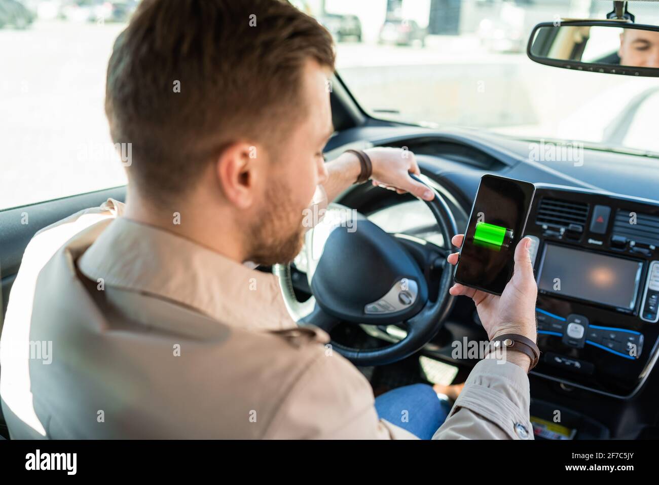 Mann beobachtet Ladeanzeige für Elektroautos über Smartphone-App. Akkustand auf dem Mobiltelefon-Bildschirm Stockfoto