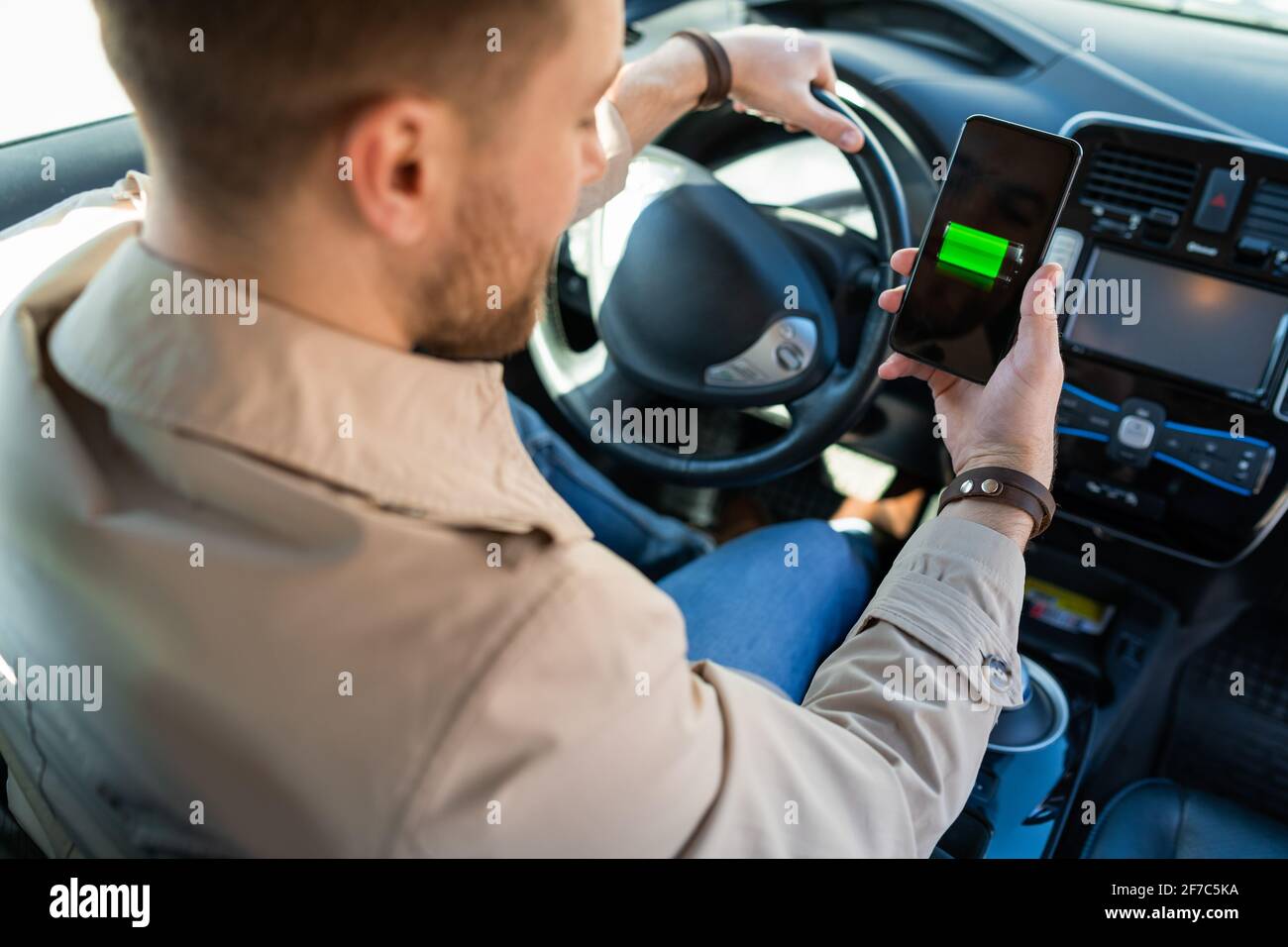 Mann beobachtet Ladeanzeige für Elektroautos über Smartphone-App. Akkustand auf dem Mobiltelefon-Bildschirm Stockfoto