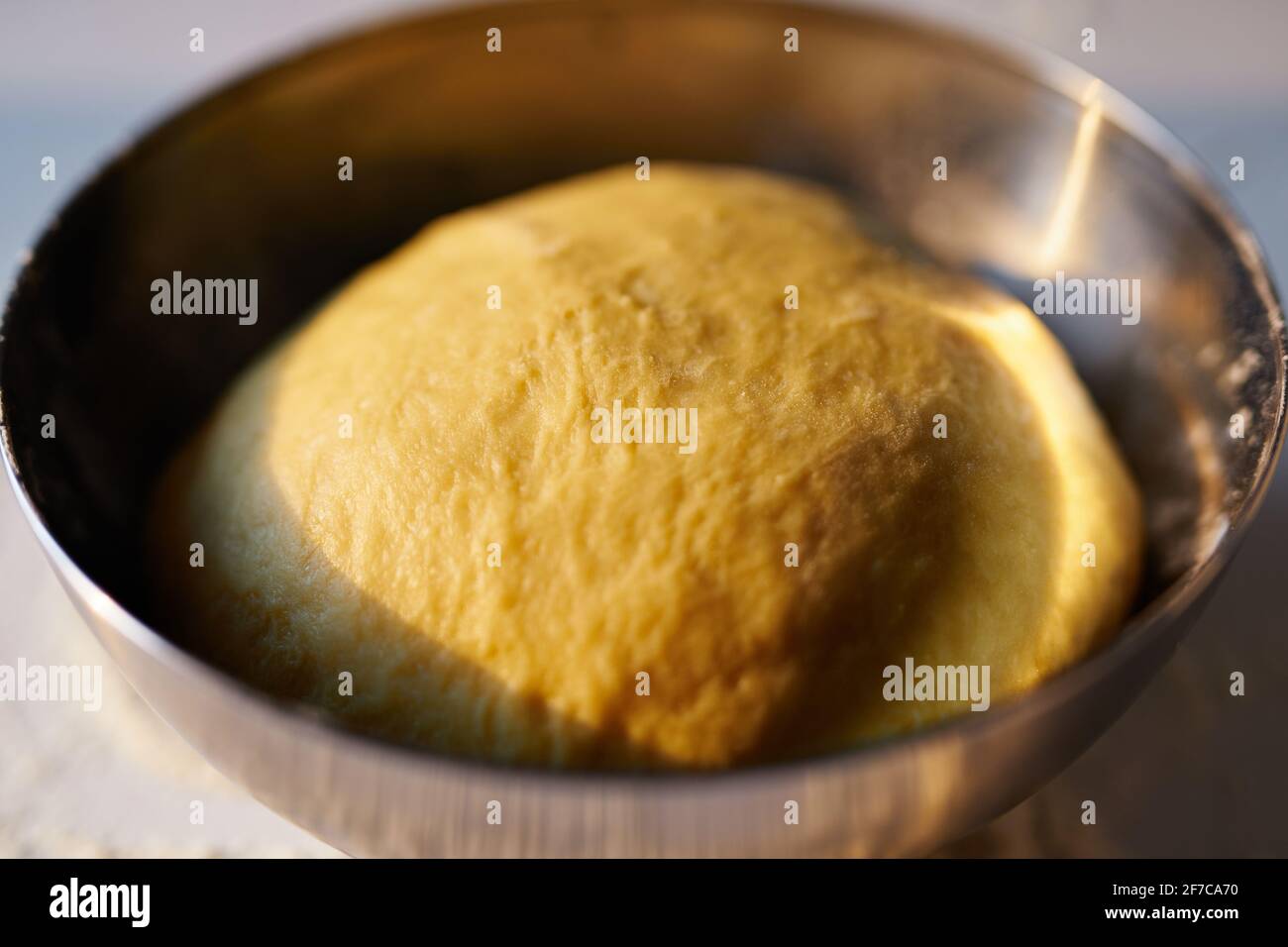 Backkonzept, Kuchen oder Ostergebäck. Frisch zubereiteter Brotteig in der Küche in Edelstahlschüssel bei Sonnenuntergang. Hochwertige Fotos Stockfoto