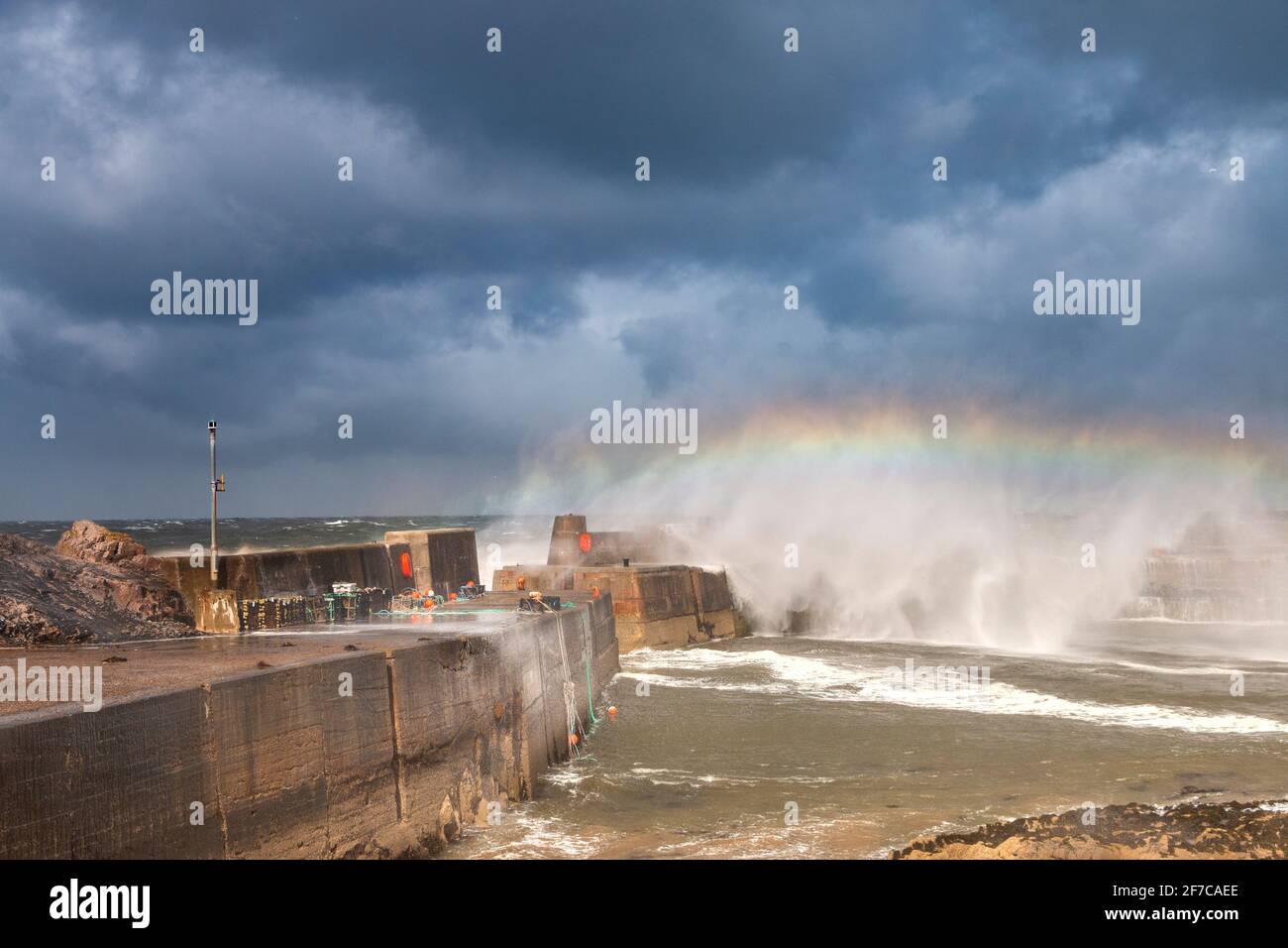 PORTKNOCKIE MORAY KÜSTE SCHOTTLAND SCHWERER STURM UND TURBULENTE WINDE UND WELLEN BRECHEN ÜBER DIE HAFENMAUER MIT EINEM REGENBOGEN IN DER SPRÜHEN Stockfoto