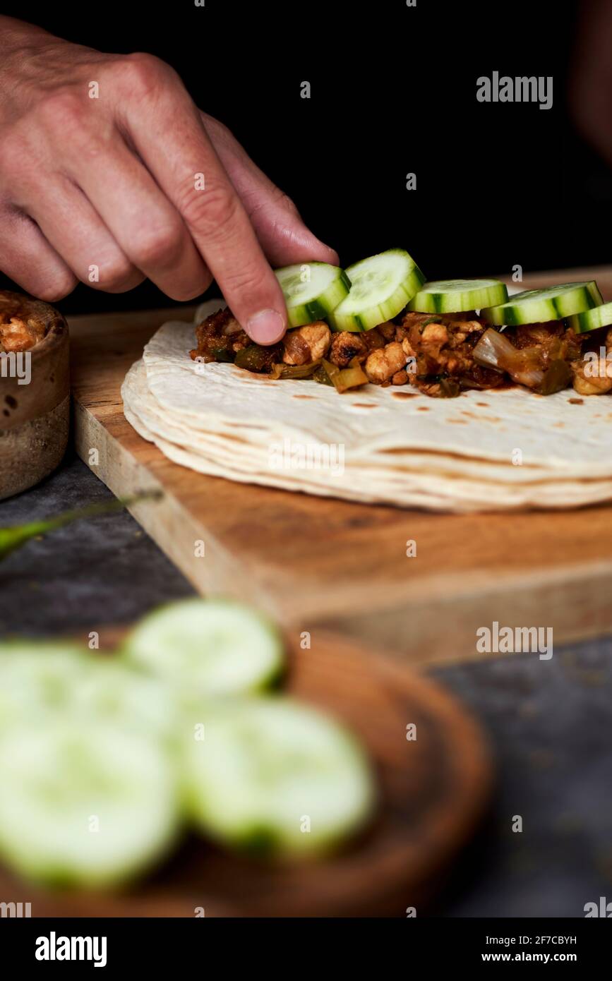 Ein junger Kaukasusmann füllt ein Durum oder einen Burrito mit Hühnerfleisch, das mit verschiedenen Gemüsesorten wie Zwiebeln oder rotem und grünem Pfeffer gekocht wird, und s Stockfoto