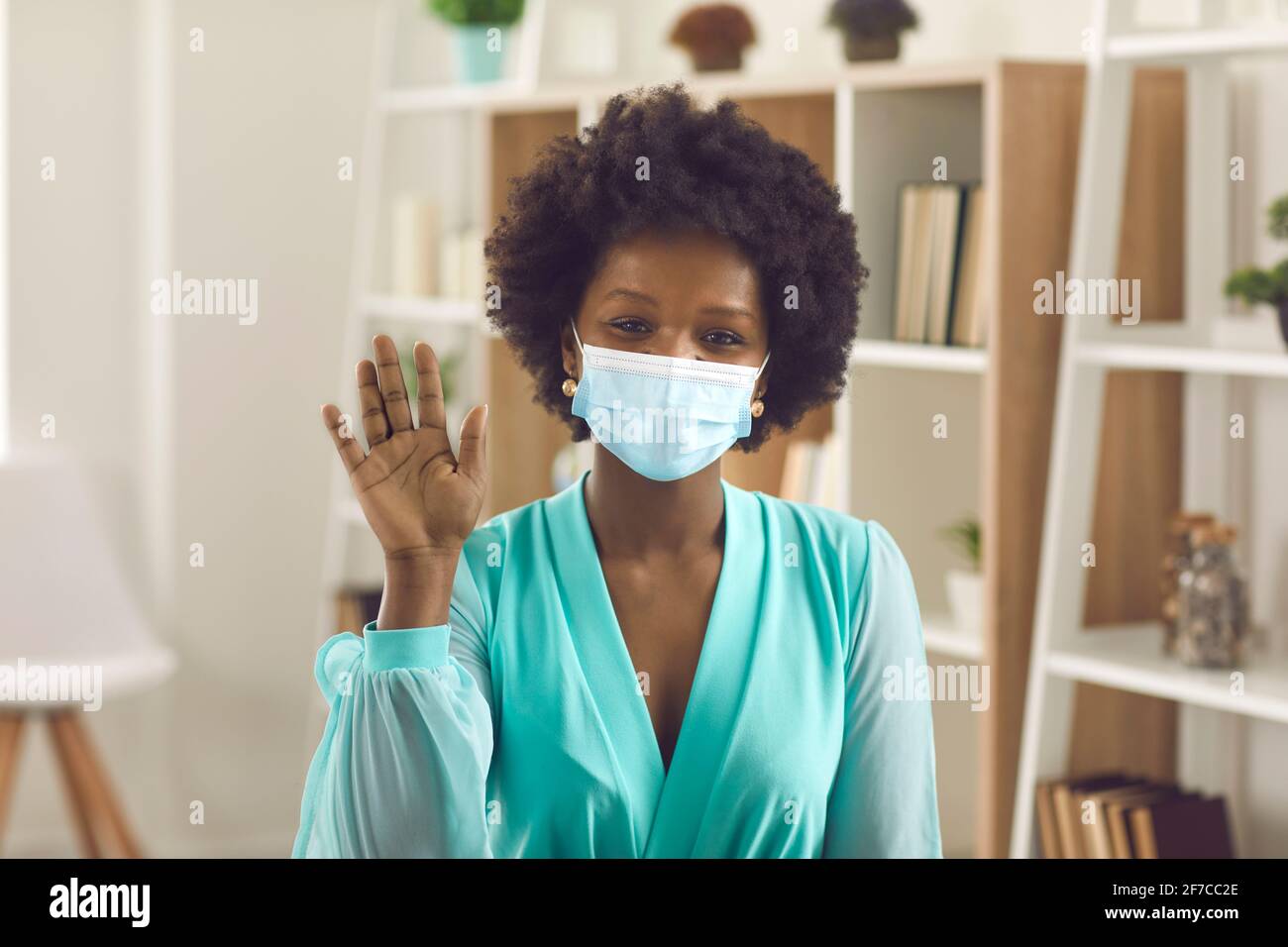 Schwarze Geschäftsfrau mit Gesichtsmaske winkt hallo Geste halten sozial Entfernung Stockfoto