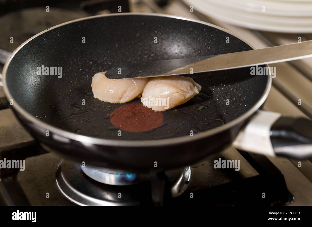 Kochen von zwei Jakobsmuscheln, die in einer Pfanne gebraten werden Auf einem Herdkochfeld Stockfoto