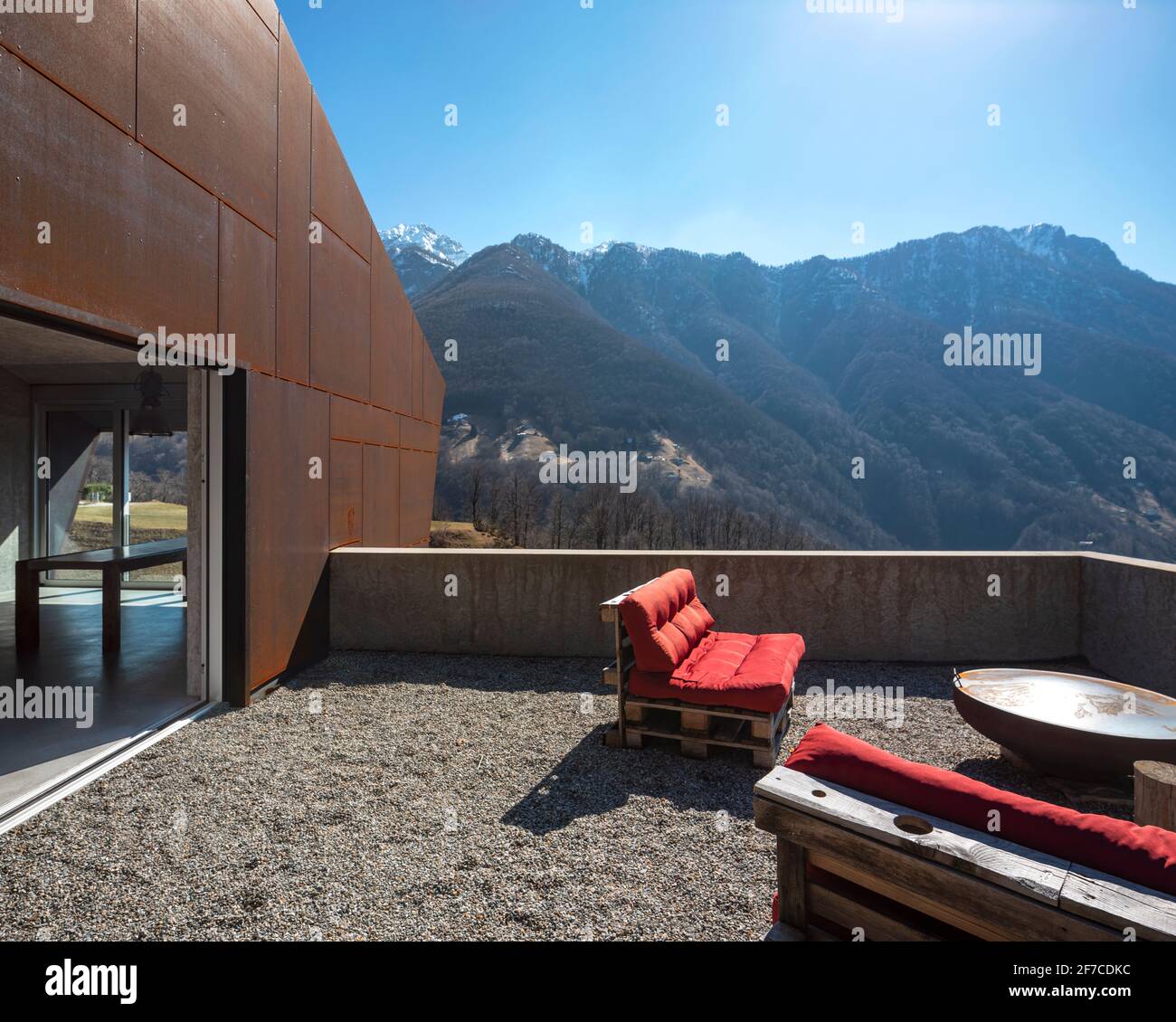 Modernes Haus mit Veranda. Rotes Sofa mit Blick auf die Berge der Schweiz. Konzept, niemand drinnen Stockfoto