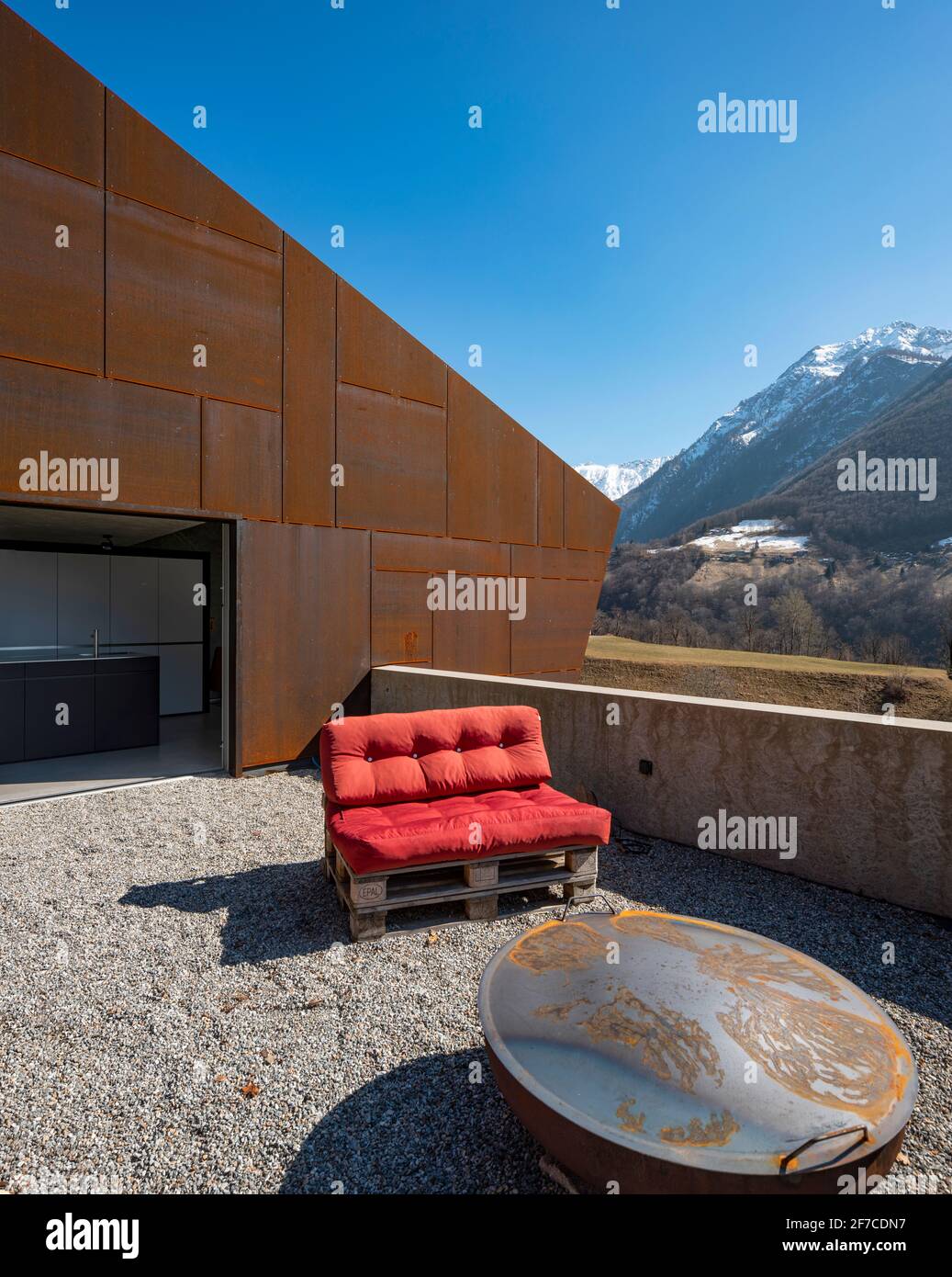 Modernes Haus mit Veranda. Rotes Sofa mit Blick auf die Berge der Schweiz. Konzept, niemand drinnen Stockfoto
