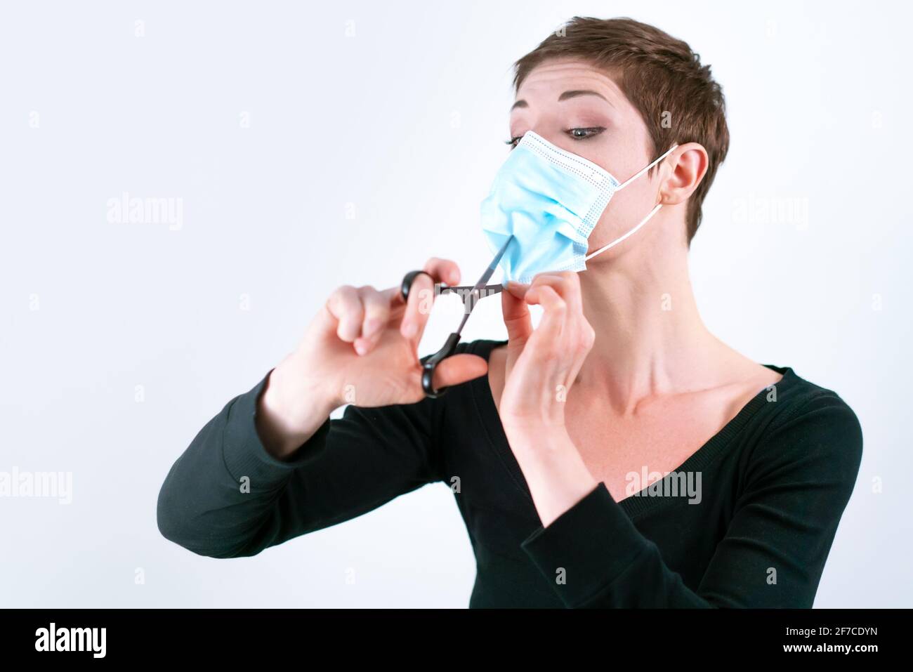 Schöne Frau mit kurzen Haaren, die ihre Gesichtsmaske mit einer Schere entfernt. Leben in Quarantäne. Umgang mit Einschränkungen des Coronavirus. Leben während einer Pandemie. Stockfoto